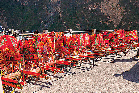 Elderly tourists or domestic tourists displaying their wealth may ride in red sedans shouldered by porters